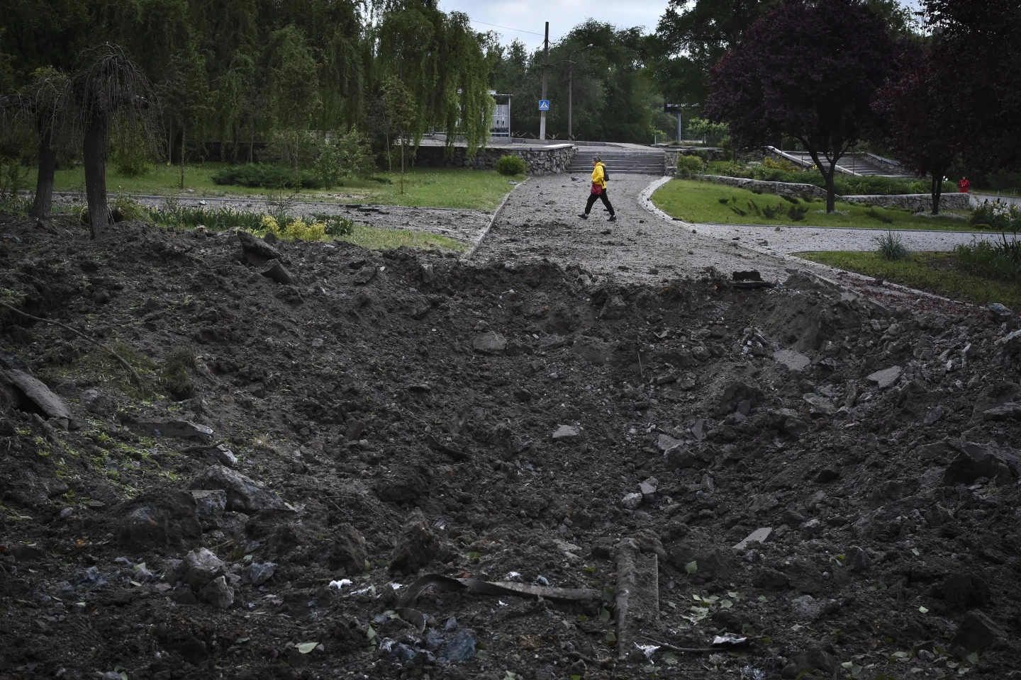 Жінка йде перед воронкою, спричиненою російським ракетним ударом, у Запоріжжі, Україна, середа, 8 травня 2024 року